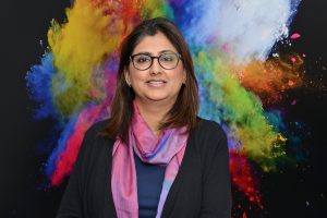 : Puneet Sandhar before a painting reminiscent of the multicultural nature of Surrey Panorama.